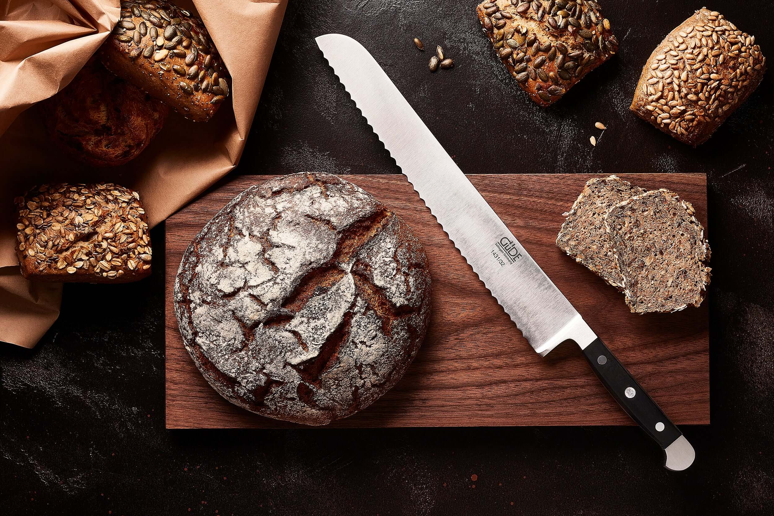 High Quality Bread Knives on a wooden board beside freshly baked bread and slices of multigrain bread.