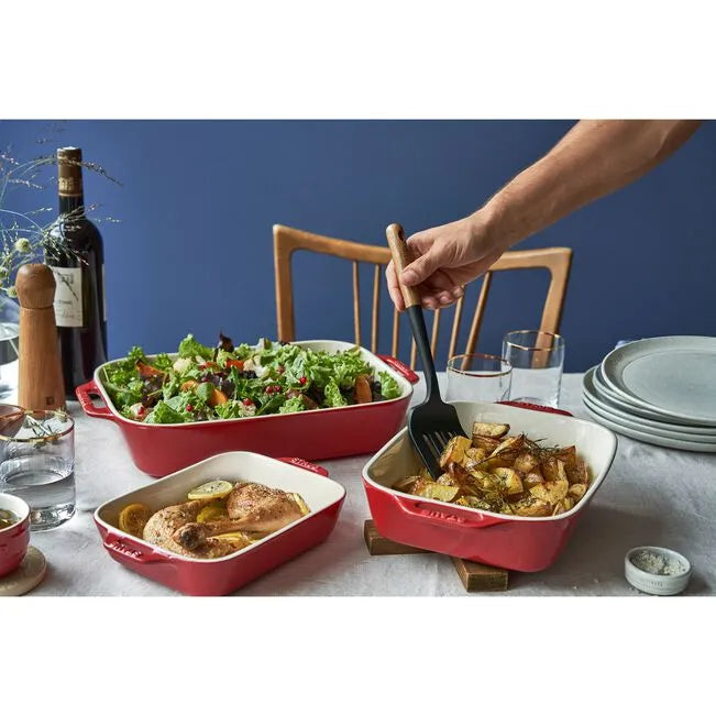 Red ceramic baking dishes with food on a table setting against a blue wall.