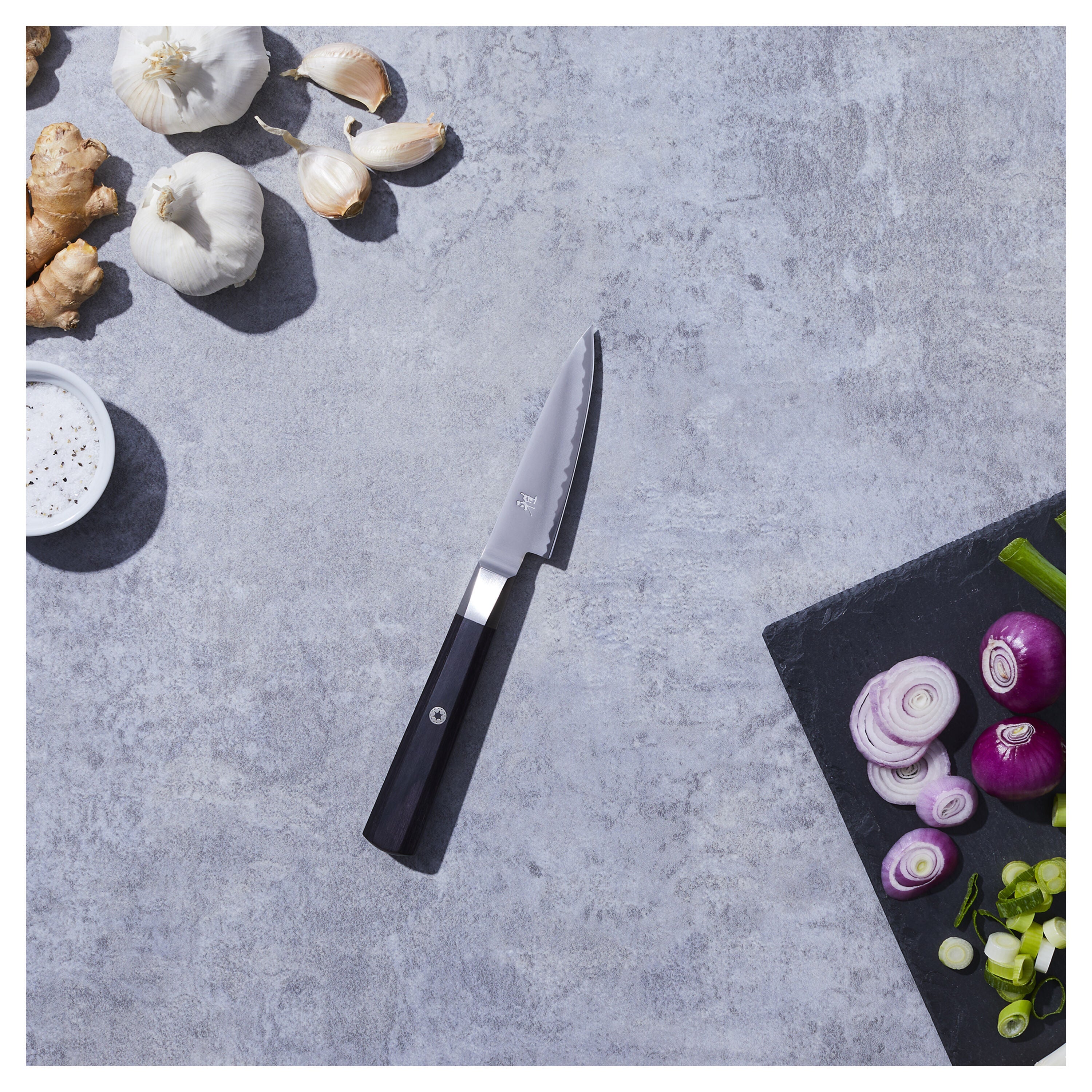 Miyabi 4000fc Japanese Kudamono Knife on a kitchen countertop with fresh garlic, ginger, and sliced vegetables.