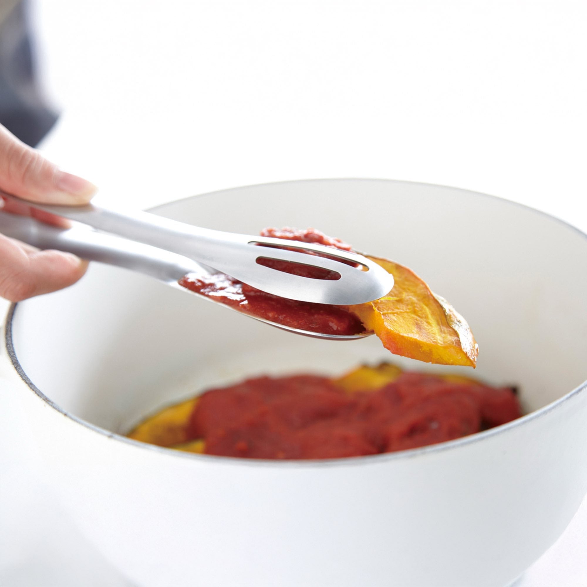 Stainless steel serving tongs lifting food from a bowl, perfect for elegant serving and cooking.