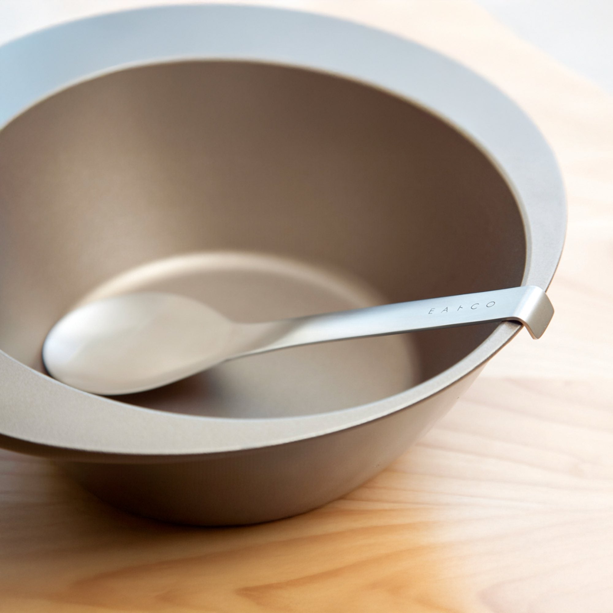 Eatoco stainless steel serving spoon resting in a sleek, modern bowl made of smooth material.