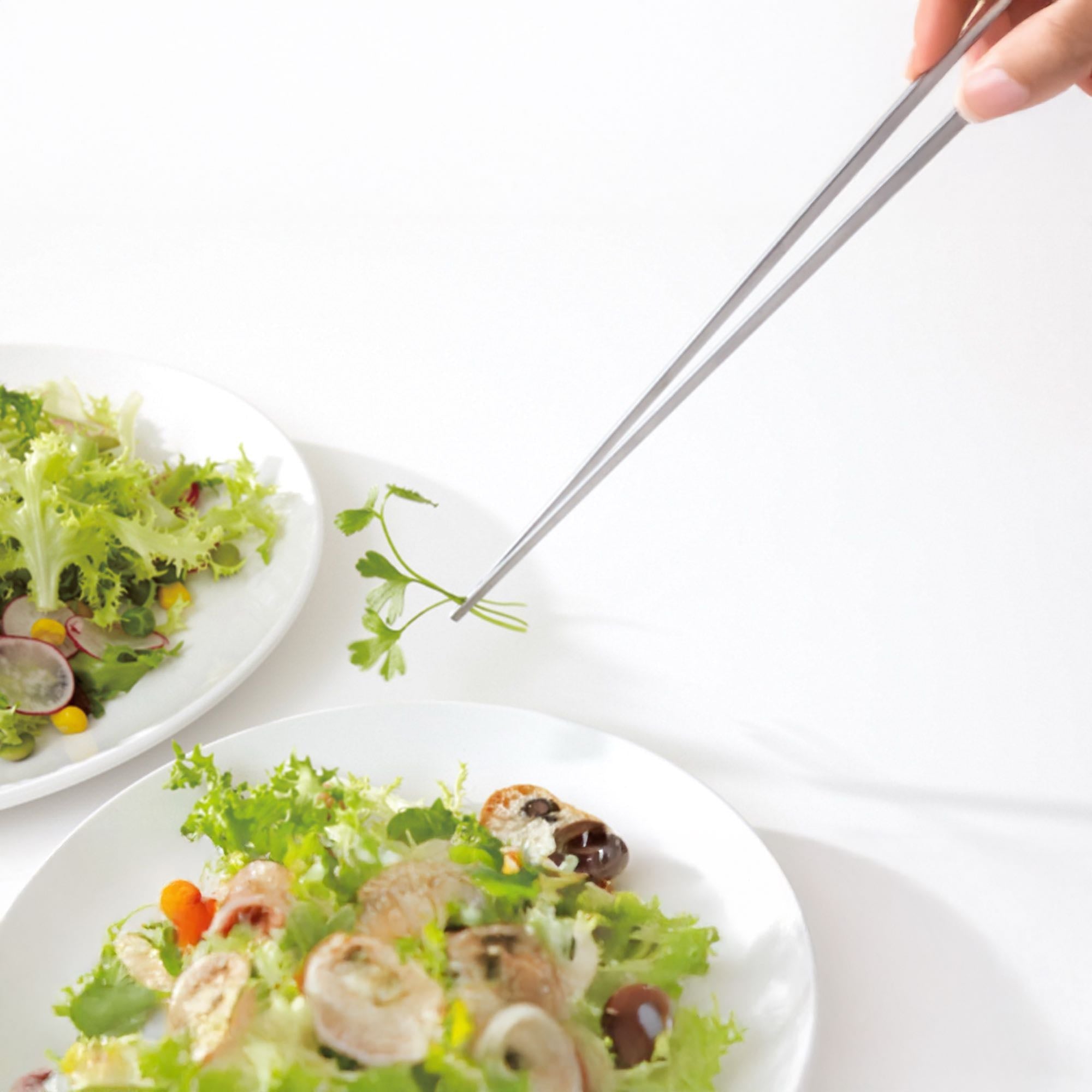 Eatoco Japan Stainless Steel Saibashi Tongs picking fresh cilantro from a salad dish.
