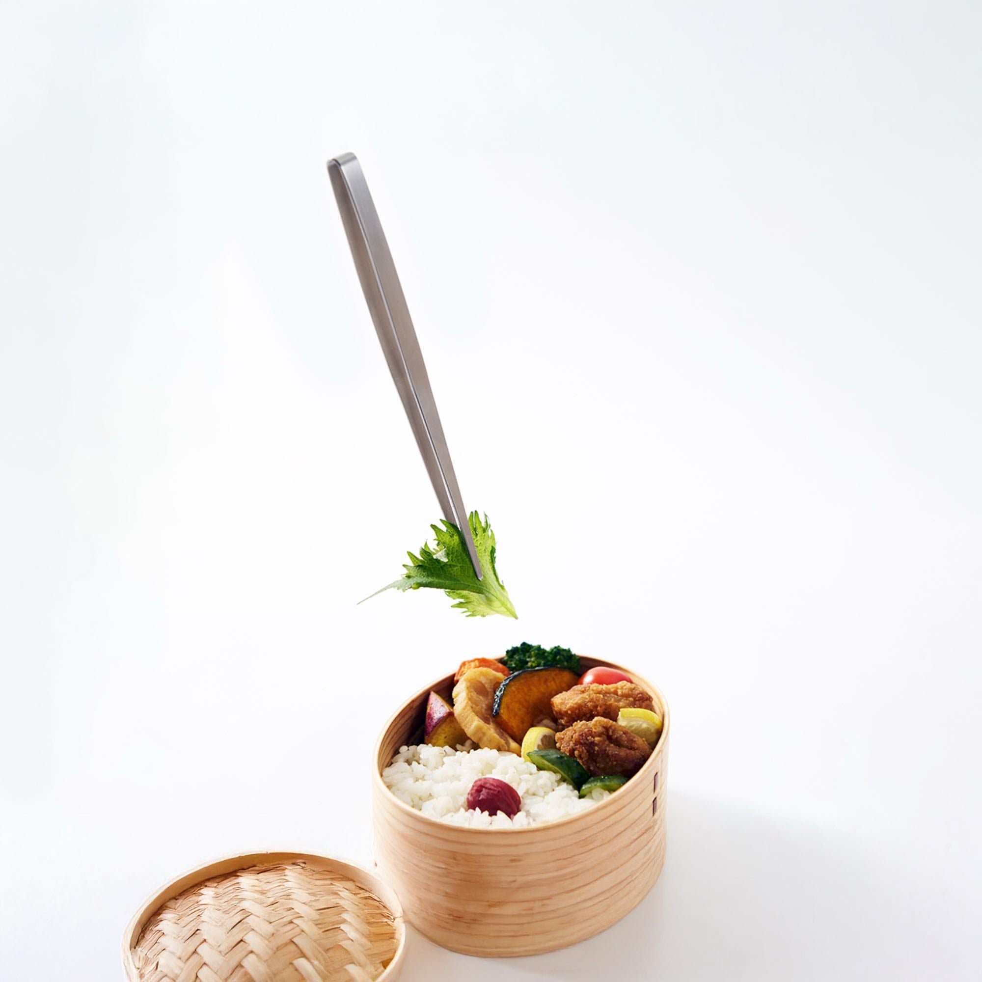 Eatoco Japan Stainless Steel Moribashi Bento Tongs lifting garnish from a bento box filled with food.