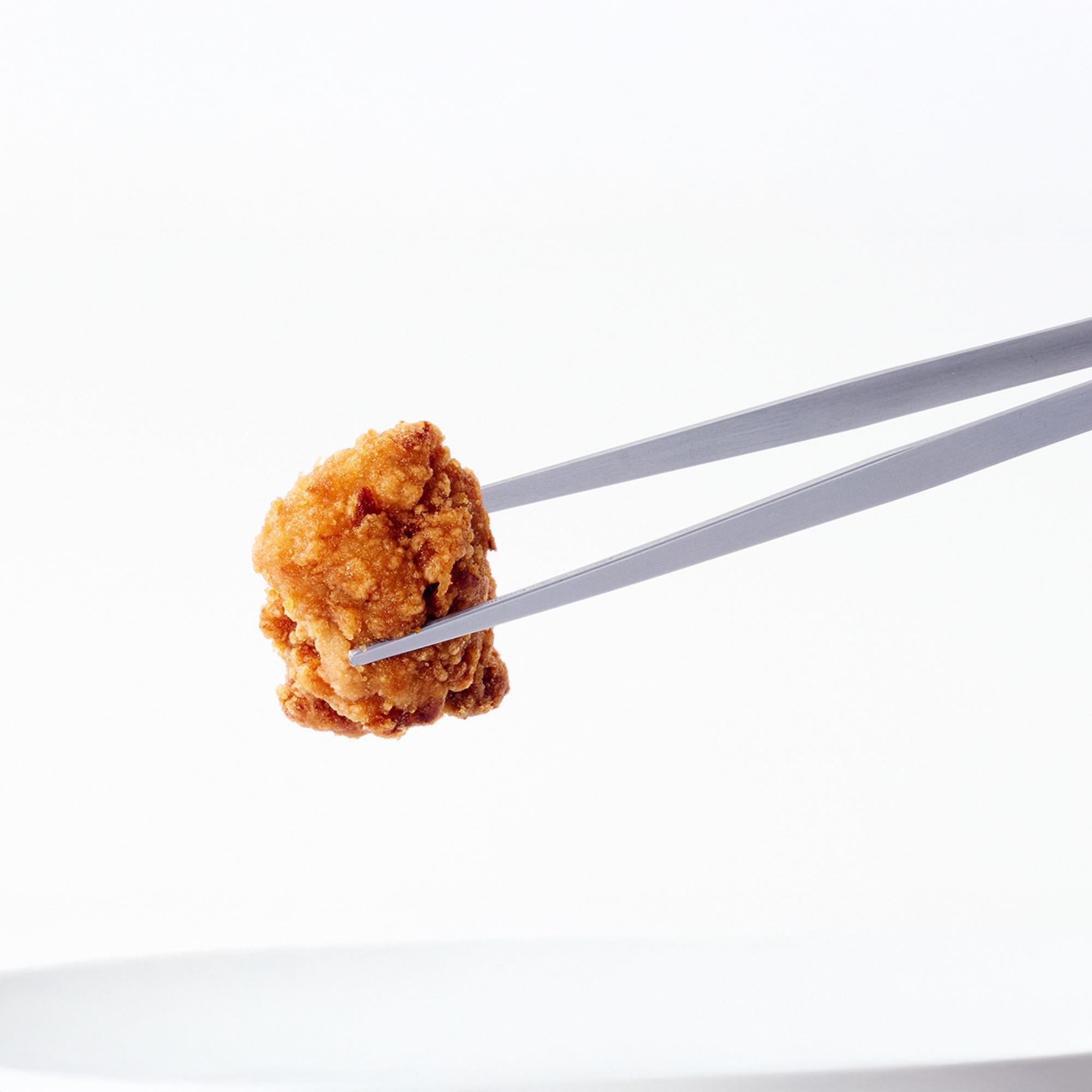 Eatoco Japan Stainless Steel Moribashi Bento Tongs holding a piece of fried chicken against a white backdrop.