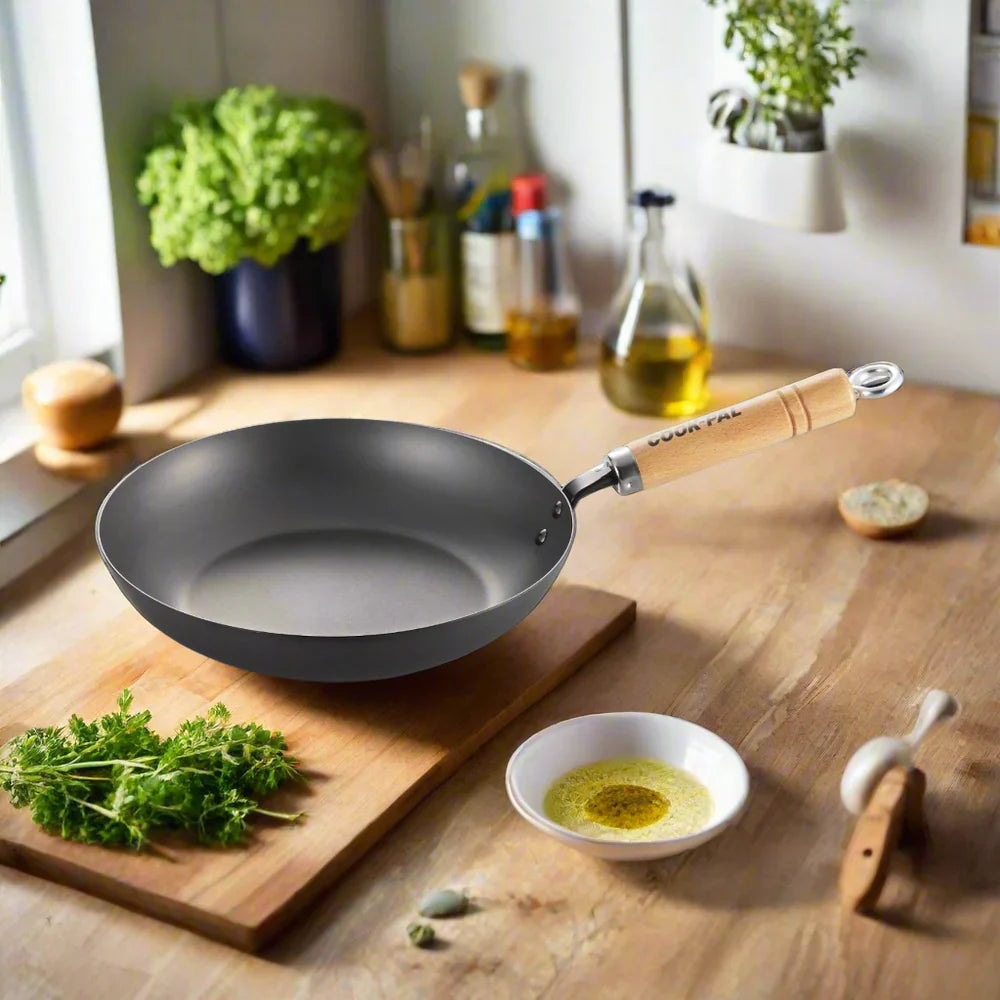 YOSHIKAWA COOK-PAL REN JAPANESE CARBON STEEL FRYING PAN with wooden handle on a kitchen counter with ingredients and utensils.