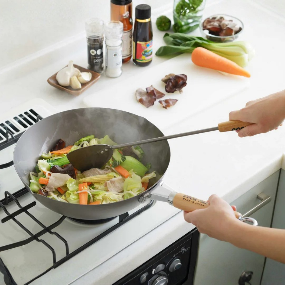 Person cooking vegetables in a wok on a stove with various ingredients around.