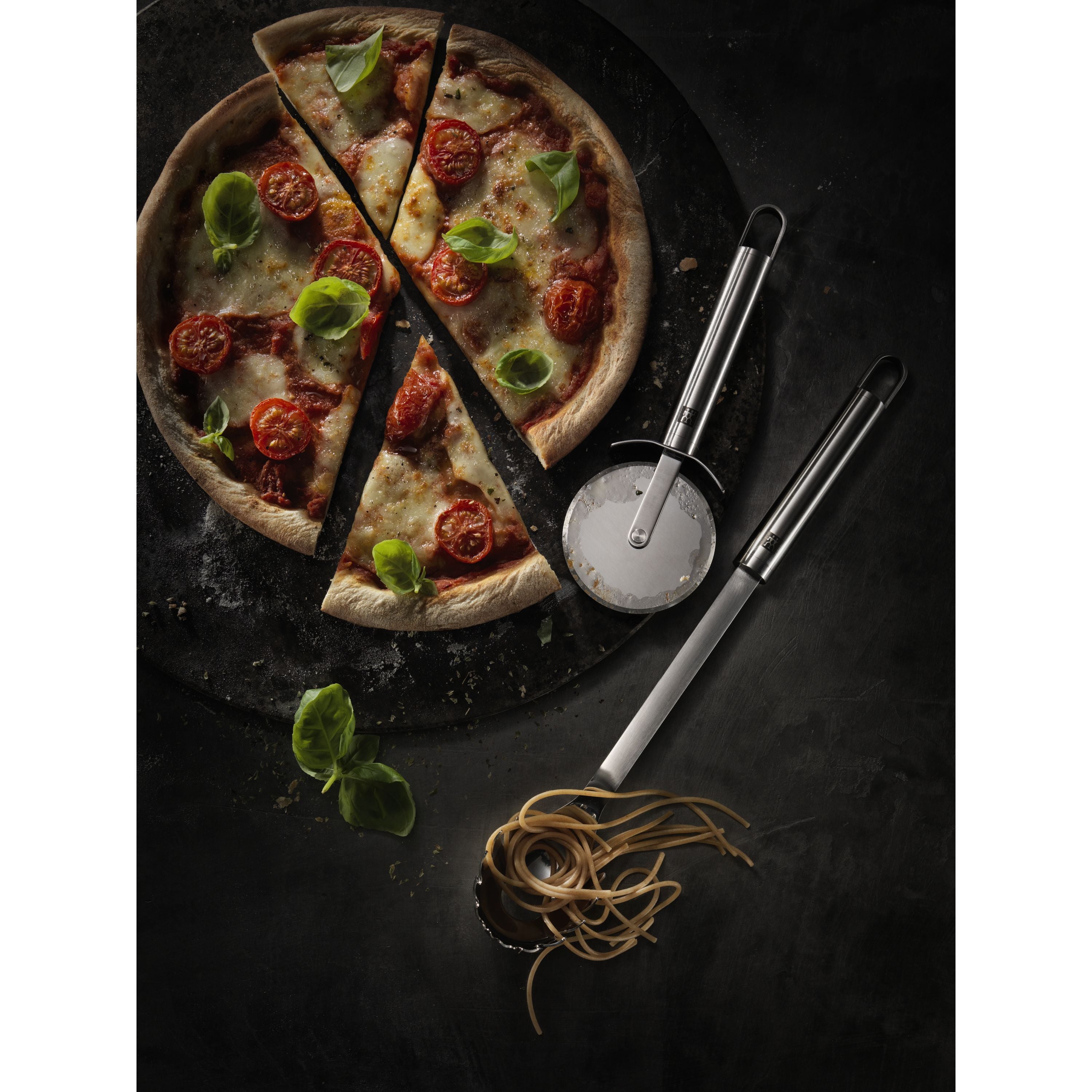 Pizza with slices cut, surrounded by pizza cutter and spoon on a dark surface