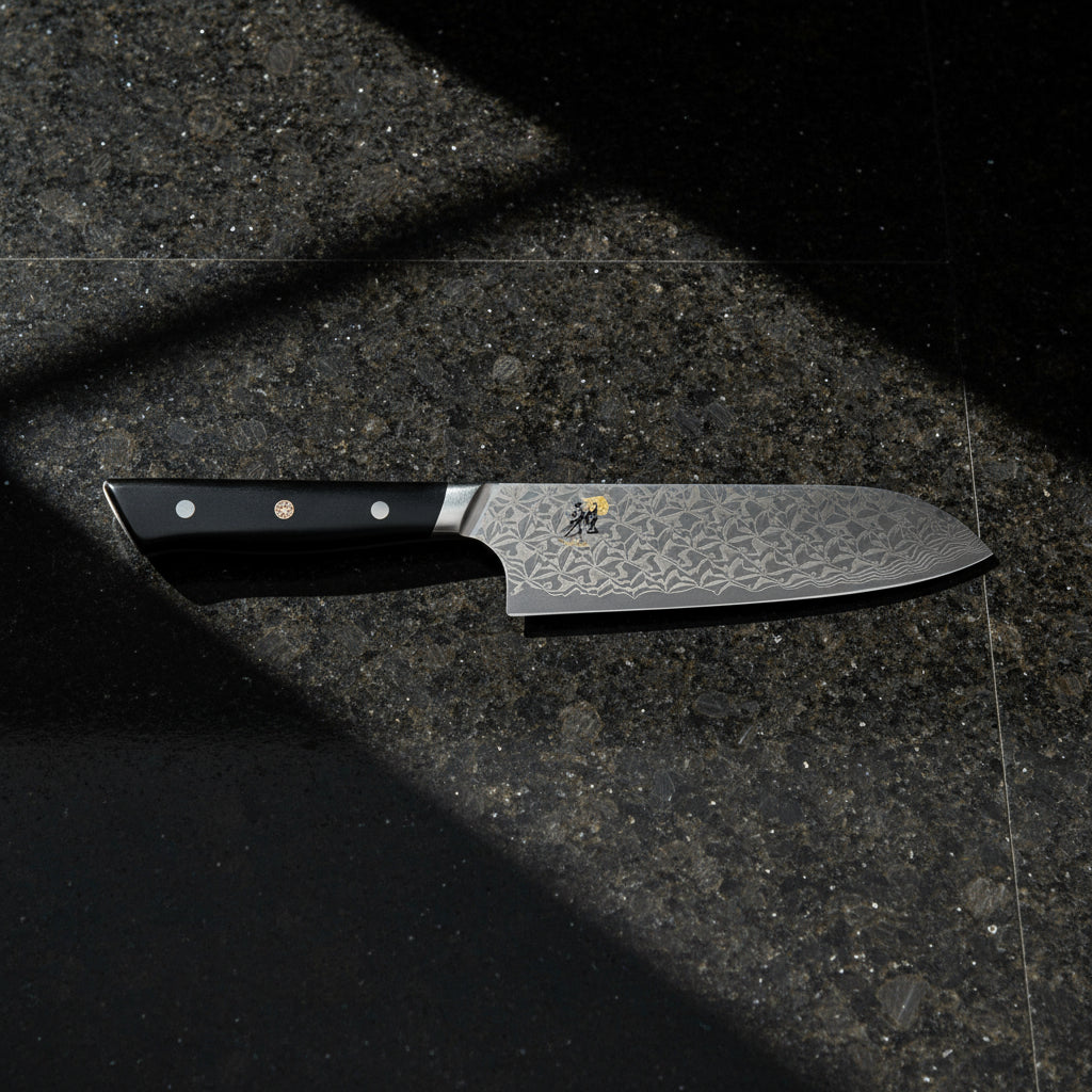 Miyabi Hibana 800DP 7-inch Santoku Damascus Steel knife on a dark countertop.