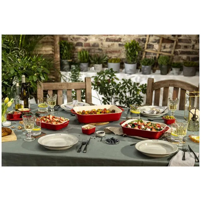 Outdoor dining table set with food, drinks, and utensils against a rustic wall and greenery.