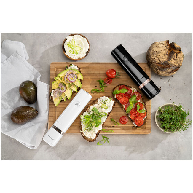 ZWILLING ENFINIGY Spice Mill alongside gourmet toast on a wooden board, highlighting its sleek design and functionality.