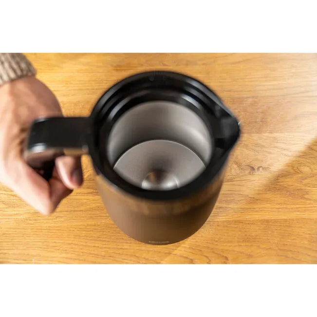 Person holding a black with silver interior thermos on a wooden surface