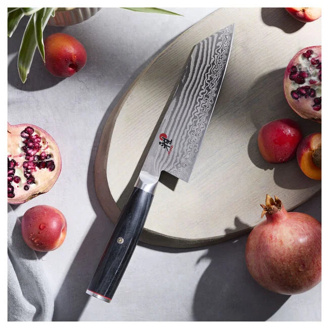 Miyabi Kaizen II 5000FCD 7-inch Bunka knife on a cutting board with pomegranates and peaches.