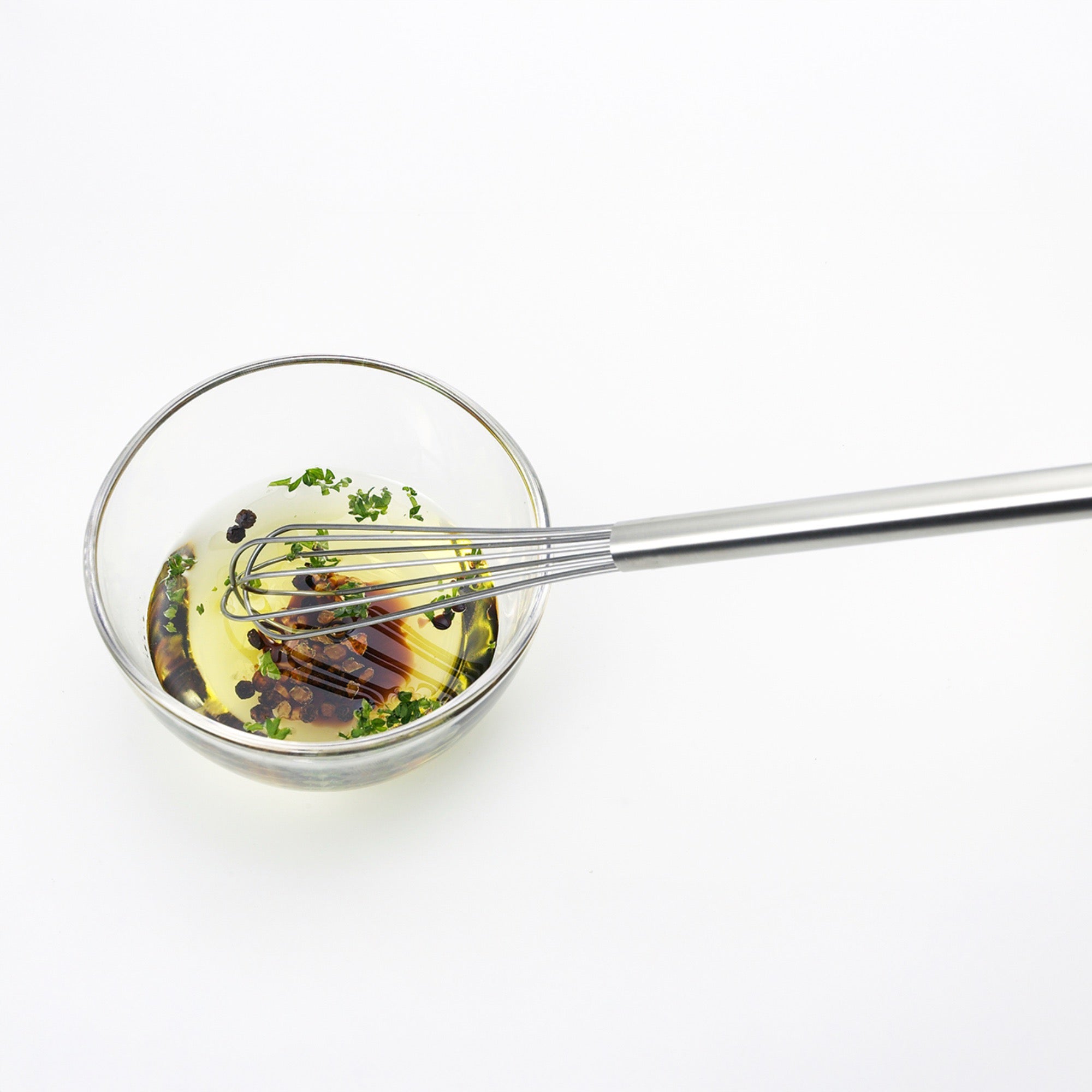 Eatoco Stainless Steel Whisk mixing oil and herbs in a glass bowl, showcasing its elegant design and functionality.