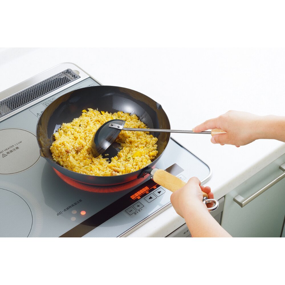 Person cooking scrambled eggs in a frying pan on an electric stove with Chinese Metal Ladle.